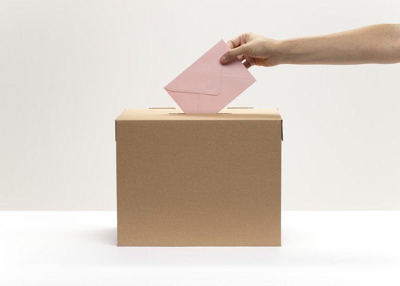 hand-puts-pink-envelope-into-vote-box