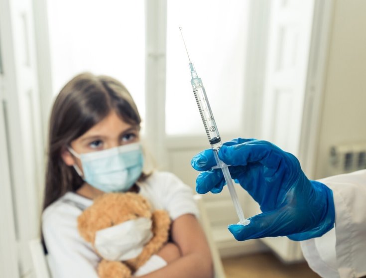 Nurse administering the coronavirus vaccine to a a young girl patient with face mask in Doctors clinic. Immunization, medical treatment and Covid-19 vaccination program after clinical trial in humans. (Nurse administering the coronavirus vaccine to a 